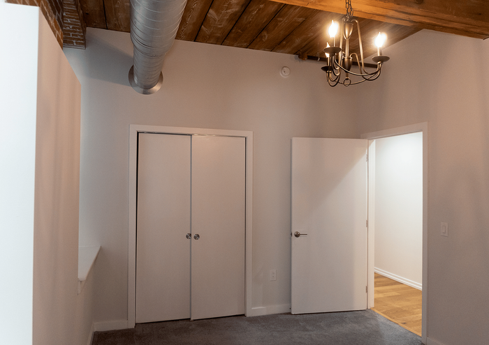 Stylish loft bedroom with exposed wooden ceiling, modern lighting, and sleek closet doors.