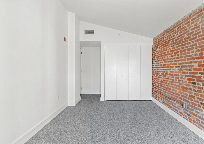 Bright apartment interior featuring a modern carpet, white walls, and a stylish exposed brick accent wall.