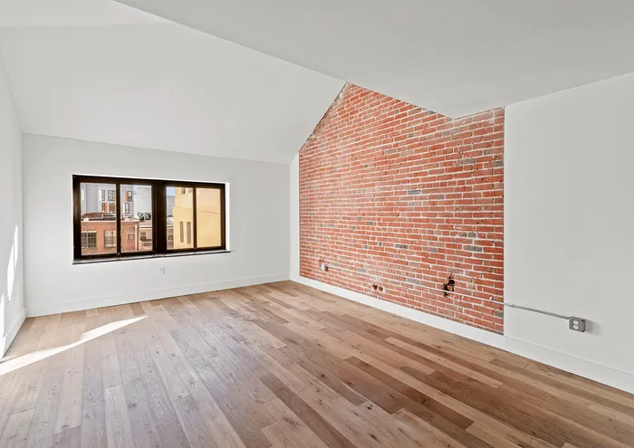 Bright urban loft with large window, brick accent wall, and hardwood flooring.