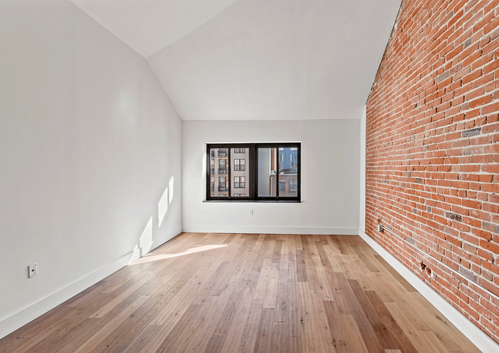 Bright loft room with wooden floor and brick accent wall.