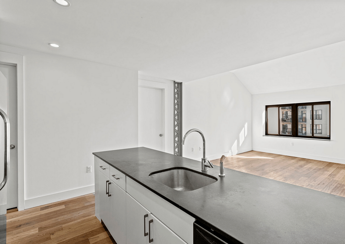 Bright modern kitchen with sleek countertops, hardwood floors, and large window.