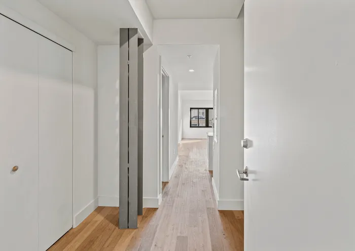 Inviting hallway with sleek wooden flooring and modern architectural details, leading to a bright space.