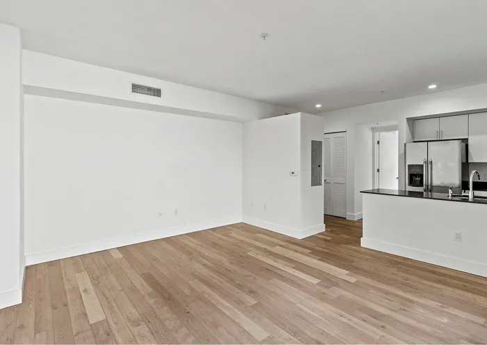 Spacious open-plan living area with hardwood floors, pristine white walls, and a modern kitchen featuring stainless steel appliances.