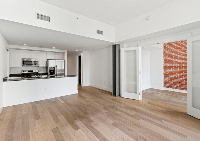 Open-concept modern apartment with sleek kitchen, spacious living area, and stylish brick accent wall.