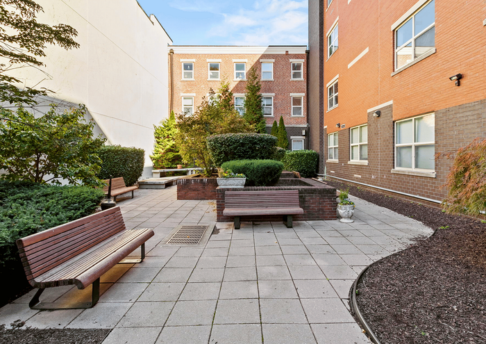 Inviting courtyard with wooden benches, lush greenery, and a peaceful atmosphere set against red-brick buildings.