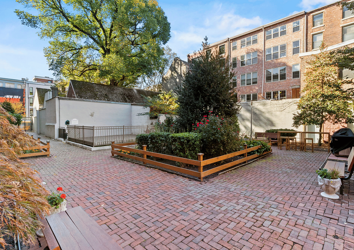 Beautiful brick courtyard featuring lush greenery and outdoor seating surrounded by urban landscape.