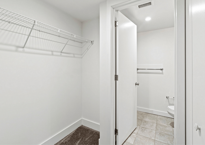 Bright walk-in closet with shelving and a glimpse of a modern bathroom.