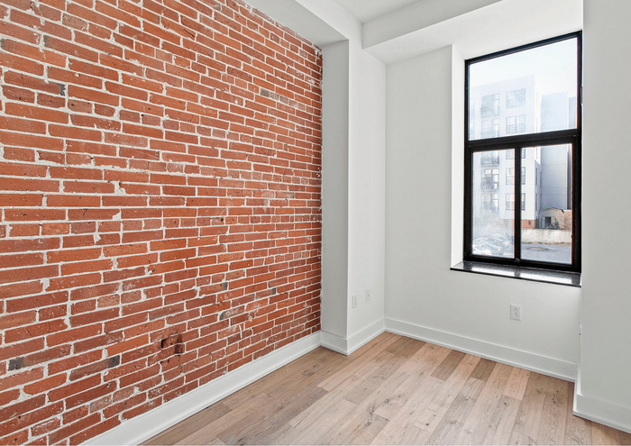 Bright room with exposed brick accent wall and large window, offering a blend of industrial and modern design.