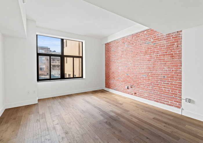 Modern apartment room with exposed brick wall and large window offering city views.