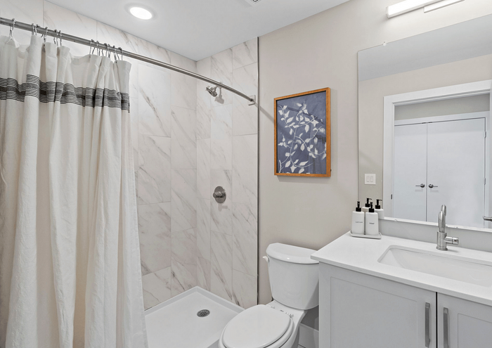 Sleek and modern bathroom with marble tile, stylish shower curtain, and framed artwork.