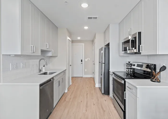 Modern kitchen with stainless steel appliances, white cabinetry, and wood flooring.