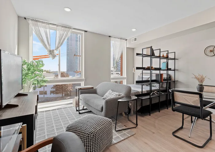 Bright and modern studio apartment with cozy seating, large windows, and stylish shelving.