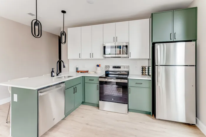 Modern kitchen with elegant green and white cabinetry, sleek stainless steel appliances, and stylish pendant lighting.