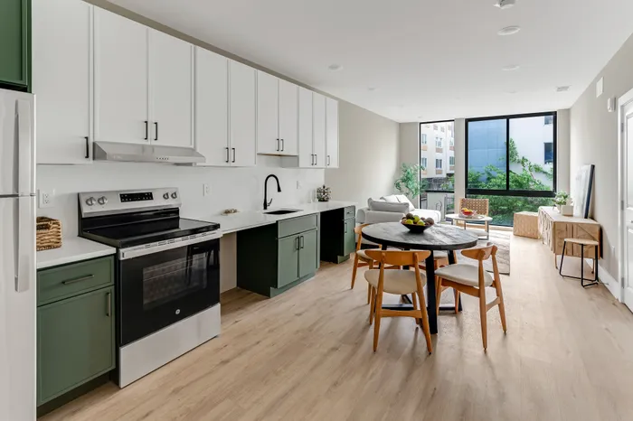 Bright, modern kitchen with sleek cabinetry and cozy dining area leading to a sunlit living room with large windows and elegant decor.