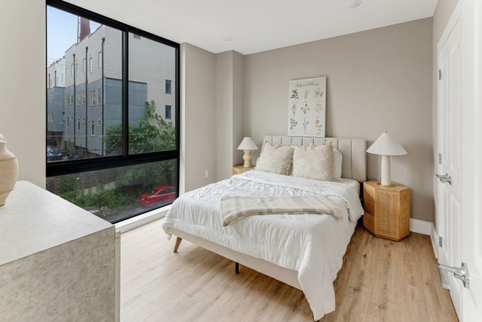 Bright and inviting bedroom with large windows, stylish decor, and cozy bedding, offering a vibrant city view and serene ambiance.
