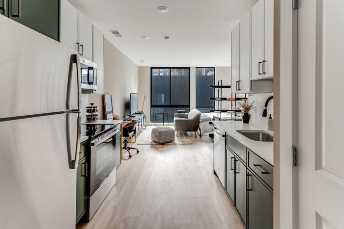 Modern open-concept apartment kitchen and living area with sleek appliances and elegant decor, featuring large windows for natural light.