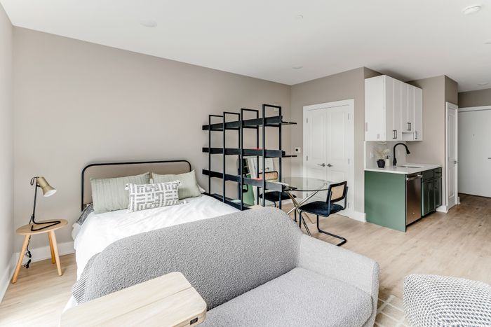 Contemporary studio apartment featuring a cozy bed, chic open shelving, a stylish kitchen with modern cabinetry, and elegant seating area, perfect for urban living.