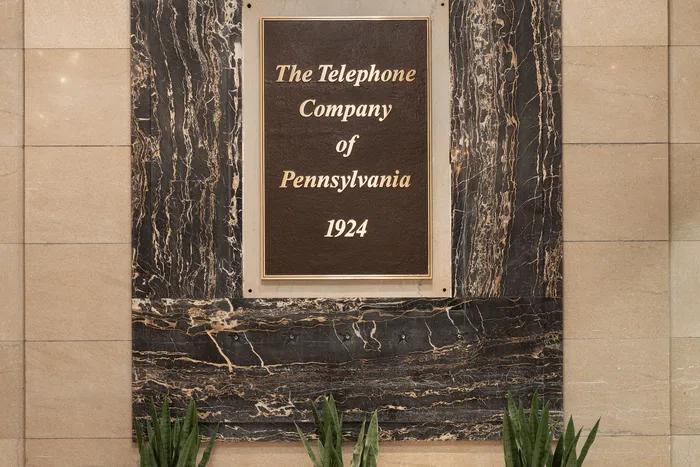 Elegant marble plaque displaying 'The Telephone Company of Pennsylvania 1924' surrounded by a stylish stone wall and green foliage.