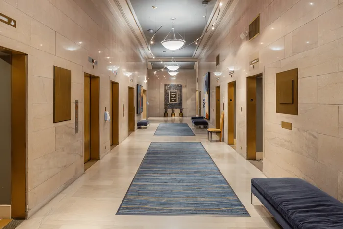 Elegant building lobby featuring sleek marble walls, multiple elevators, and modern artwork with ambient lighting.