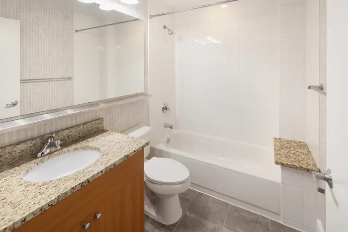 Modern bathroom with sleek granite countertop, elegant wooden cabinetry, and pristine white tiles.