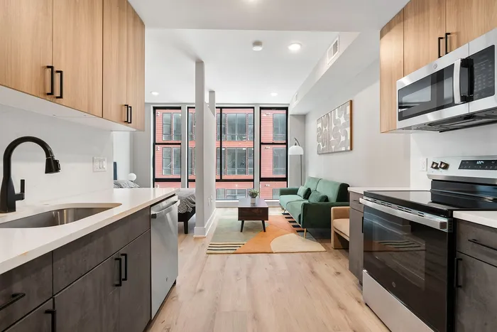Modern open-plan apartment featuring a sleek kitchen with dark cabinets, flowing into a stylish living area with a green sofa and large windows offering abundant natural light.