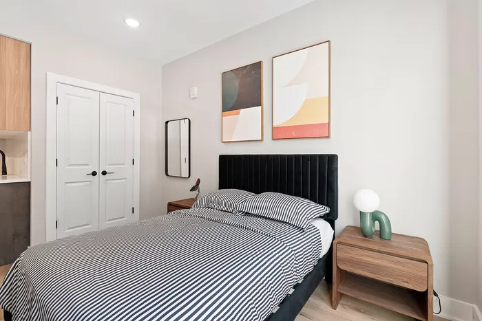 Bright and modern bedroom with stylish wall art, sleek black velvet headboard, and minimalistic wooden nightstand.