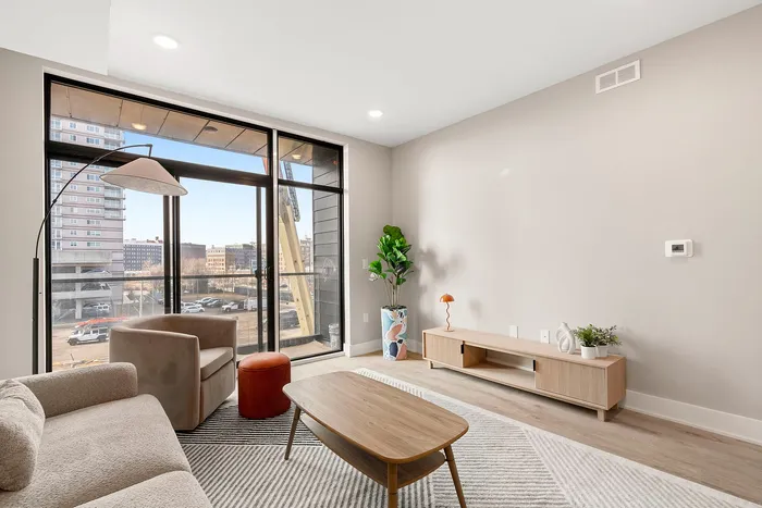 Elegant living room with modern furniture, large glass windows offering a vibrant cityscape view, and chic decor accents.