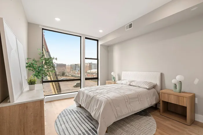 Bright and modern bedroom with large windows, cozy bed, and chic decor overlooking a cityscape.
