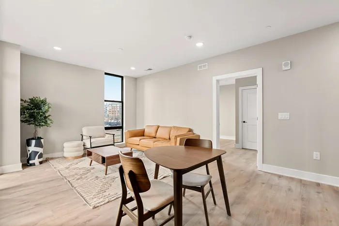Bright and modern living room with a cozy leather sofa, elegant wooden chairs, and a stylish potted plant, perfect for relaxation and entertaining.
