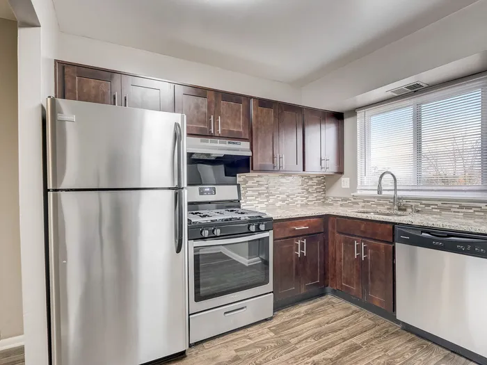 Modern kitchen with stainless steel appliances, elegant dark wood cabinets, and natural light streaming in through a large window.