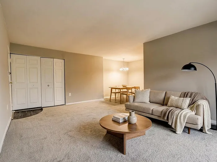 Inviting living space with elegant beige sofa, cozy throw, sleek wooden coffee table, and a chic dining area under stylish lighting.