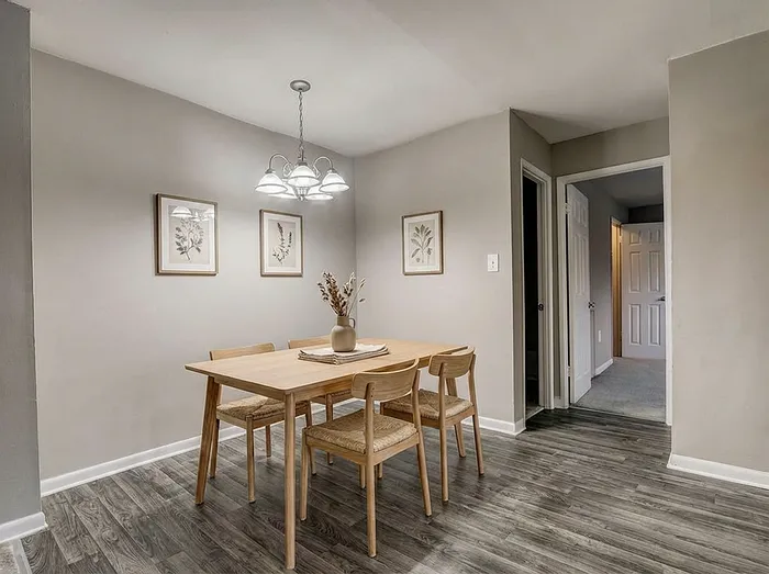 Elegant dining room with modern wooden table and chairs, bathed in soft lighting, accented by botanical wall art and stylish gray flooring.