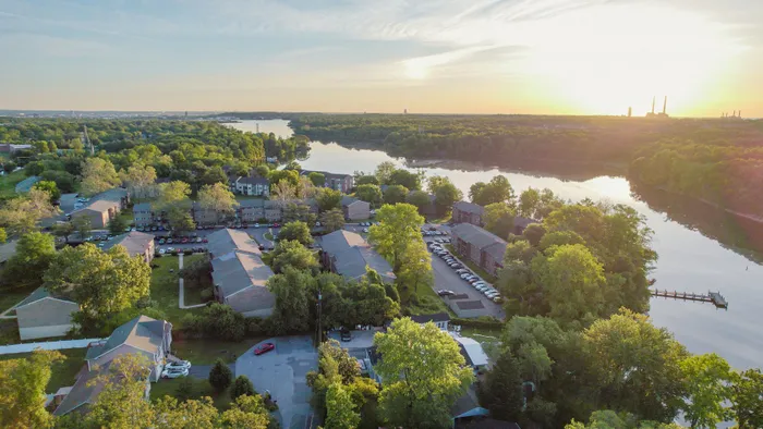 Breathtaking aerial view of riverside apartment complex surrounded by lush greenery, offering serene living with natural beauty and stunning sunset views.