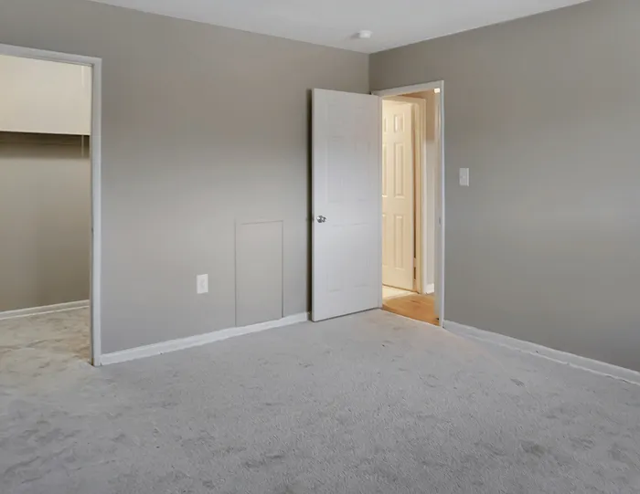 Inviting bedroom with soft carpet flooring and neutral wall tones, featuring two doorways leading to a walk-in closet and a bright hallway.