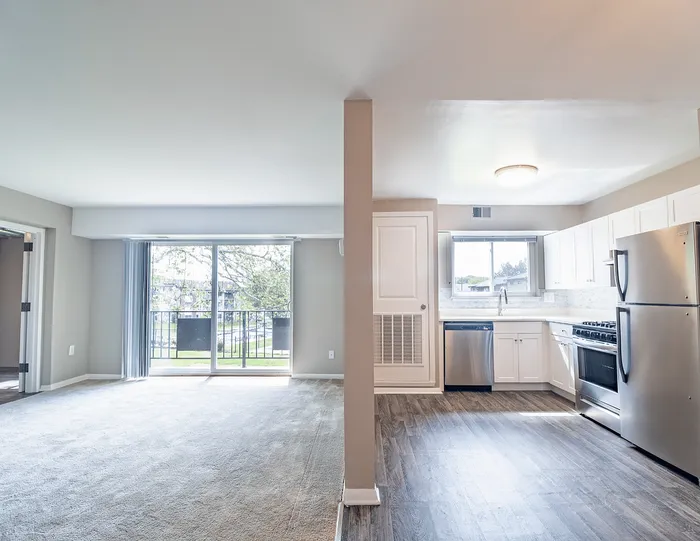 Bright open-plan living room and kitchen with modern stainless steel appliances, large windows, and elegant flooring.