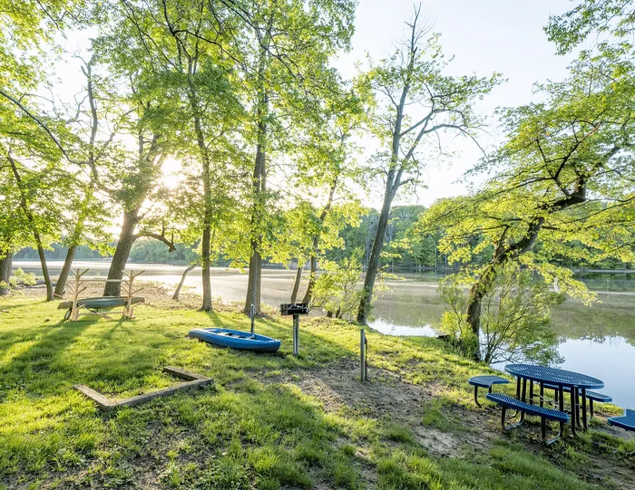 Serene riverside retreat with lush greenery, a cozy campfire area, and picturesque morning light reflecting off the water.