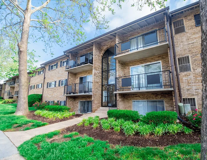 Charming brick apartment complex with private balconies, lush landscaping, and serene pathways.