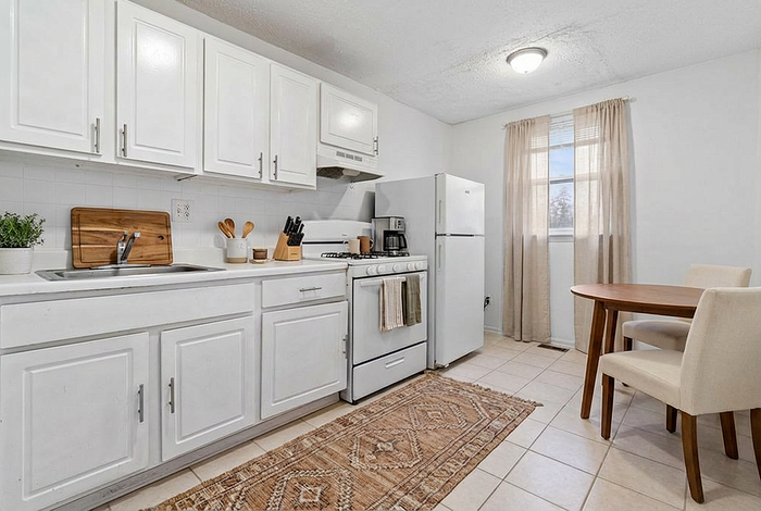 Bright and inviting kitchen with modern white cabinets, cozy dining area, and natural light streaming through a large window.