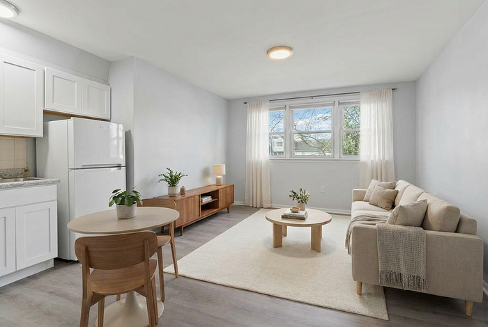 Charming open-plan living area with a cozy beige sofa, natural wood furniture, and bright spacious windows, perfect for relaxation.