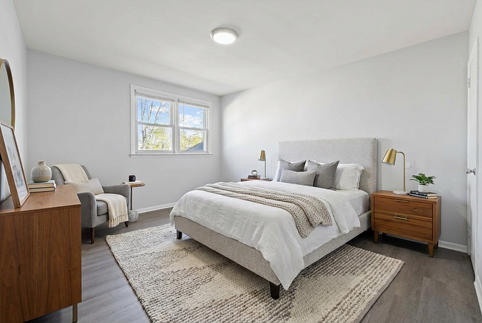 Inviting bedroom with a plush bed, contemporary furniture, and natural light streaming through a large window.