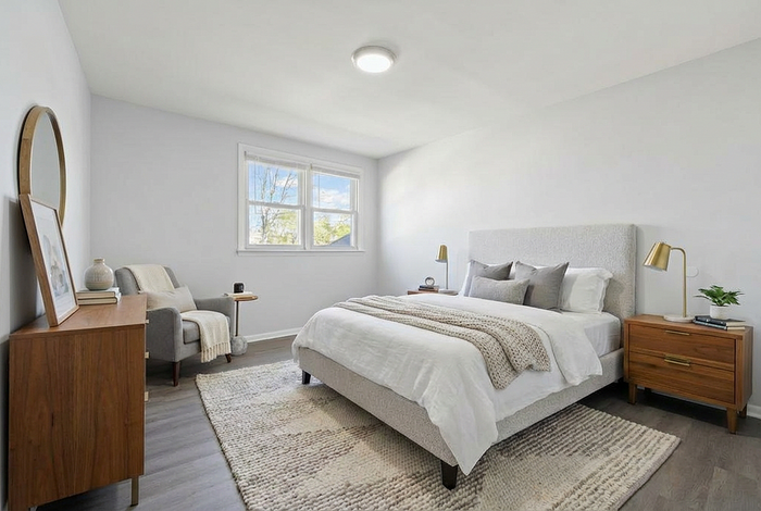 Elegantly designed bedroom featuring a plush bed with cozy blankets, stylish wooden furniture, and ample natural light from a large window.