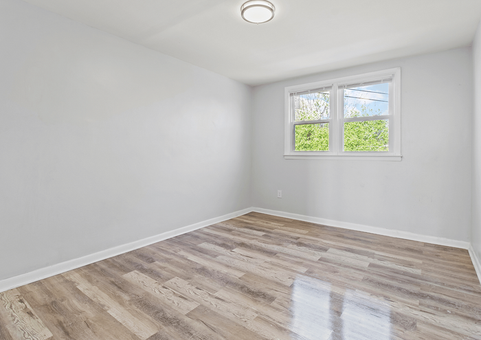 Bright and airy bedroom with sleek hardwood floors, large double windows, and fresh white walls, perfect for personalization.