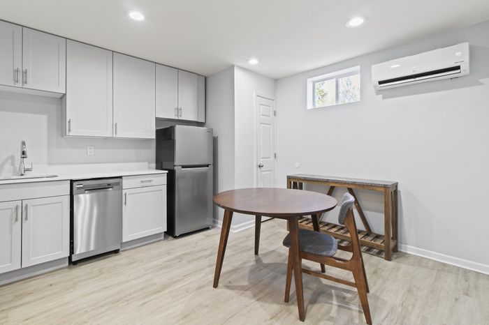 Modern kitchen with sleek white cabinets, stainless steel appliances, and a cozy dining area with a stylish wooden table and chair.