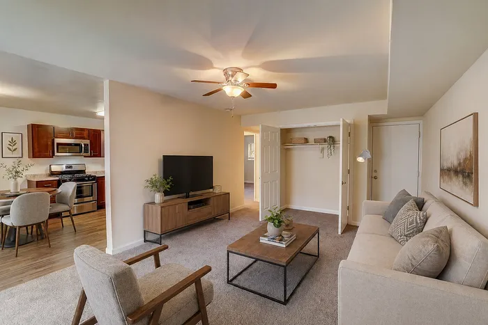 Inviting living room with plush carpeting, stylish furniture, and a glimpse into a modern kitchen with stainless steel appliances.