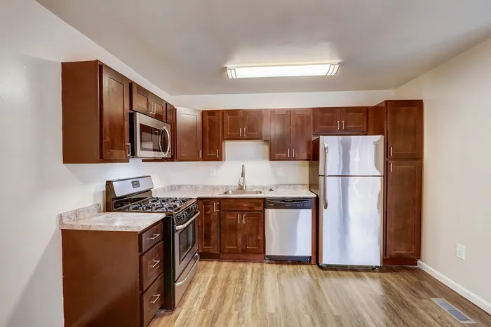Modern kitchen with rich wood cabinetry, sleek stainless steel appliances, and elegant stone countertops.