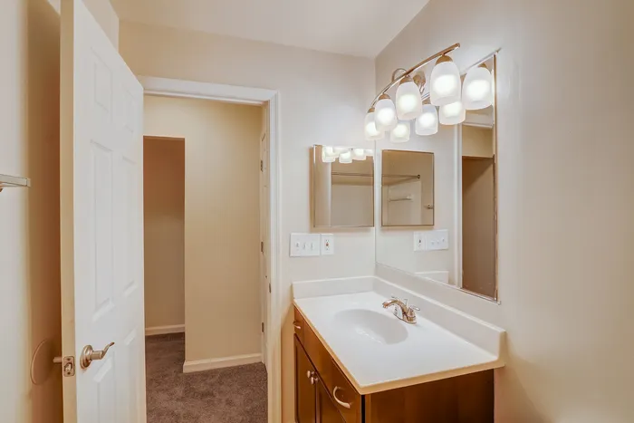 Modern bathroom with elegant lighting, sleek mirror, and chic wooden vanity, creating an inviting and stylish atmosphere.