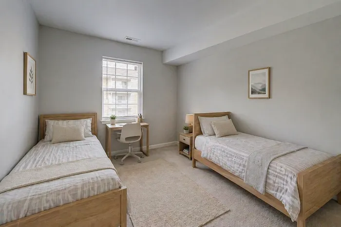 Bright, cozy bedroom with two twin beds, modern wooden furniture, and a window providing natural light.