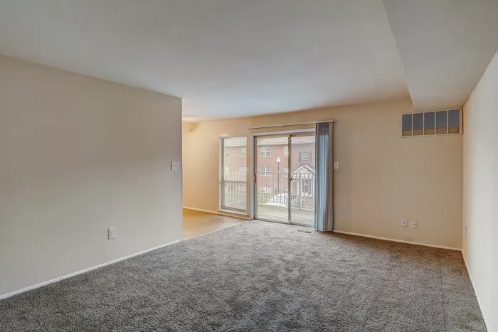 Bright and spacious living room with plush carpeting and large sliding doors leading to a private balcony.