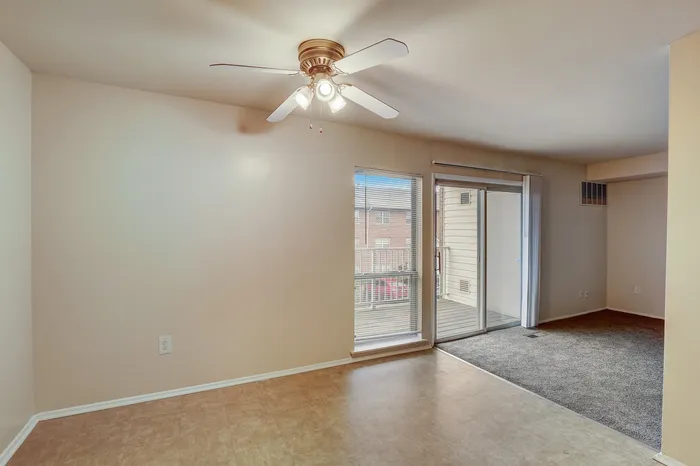 Bright, open living space with a ceiling fan, large window, and sliding glass door leading to a private balcony.