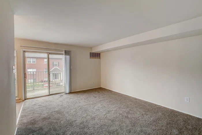 Inviting open living space with plush carpet and sliding glass doors leading to a private balcony view.